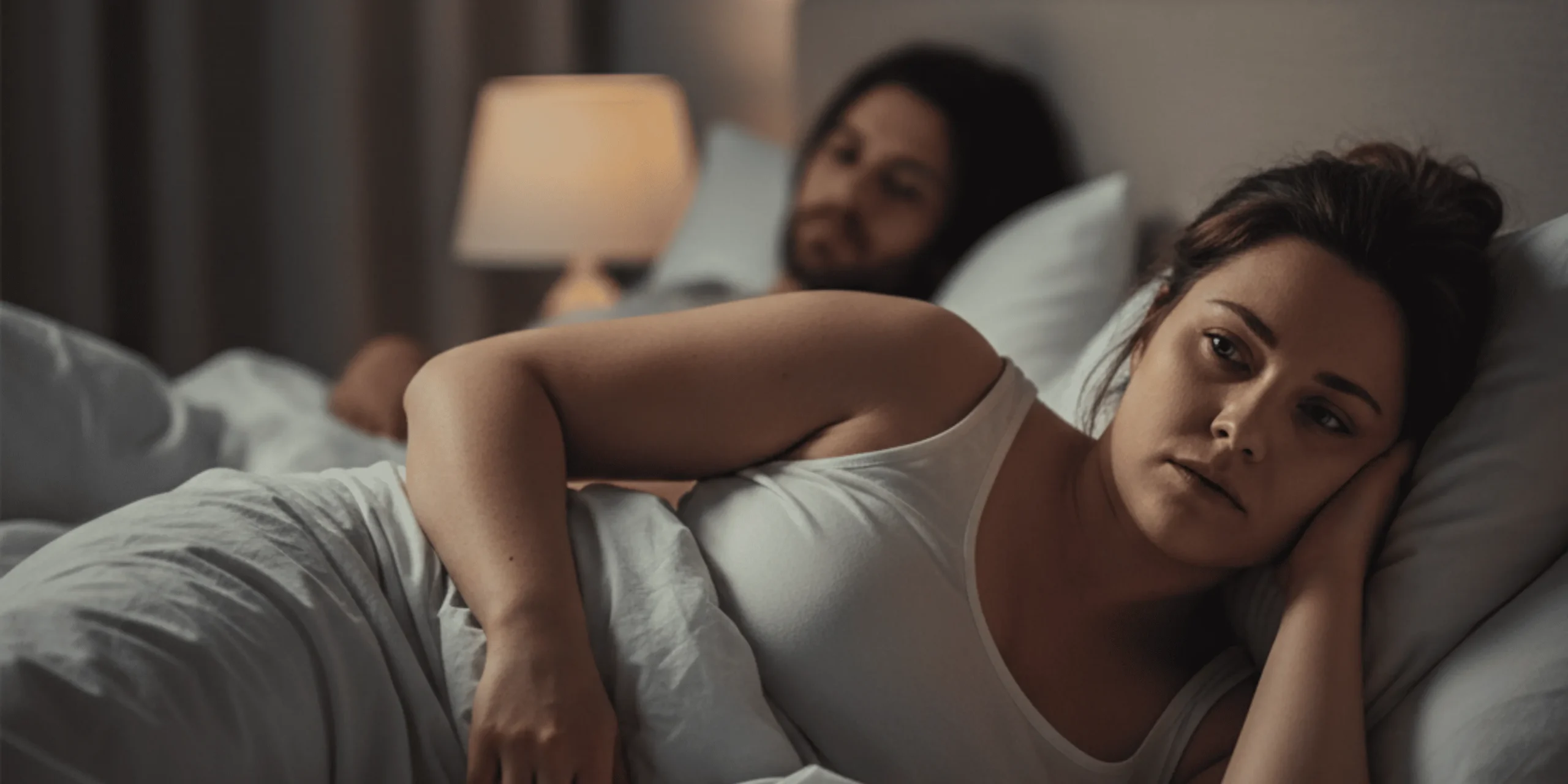 Mujer en la cama dando la espalda a su pareja, sintiéndose culpable y cansada